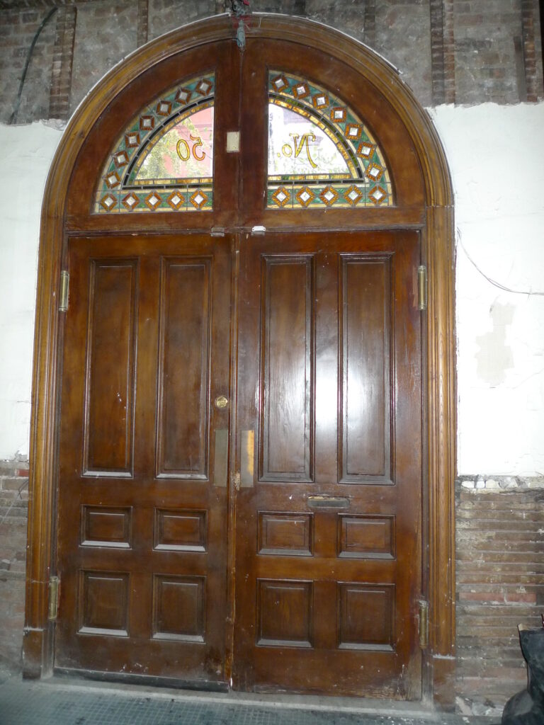 Restored arched wood entrance door with a leaded stained-glass transom in a historic building