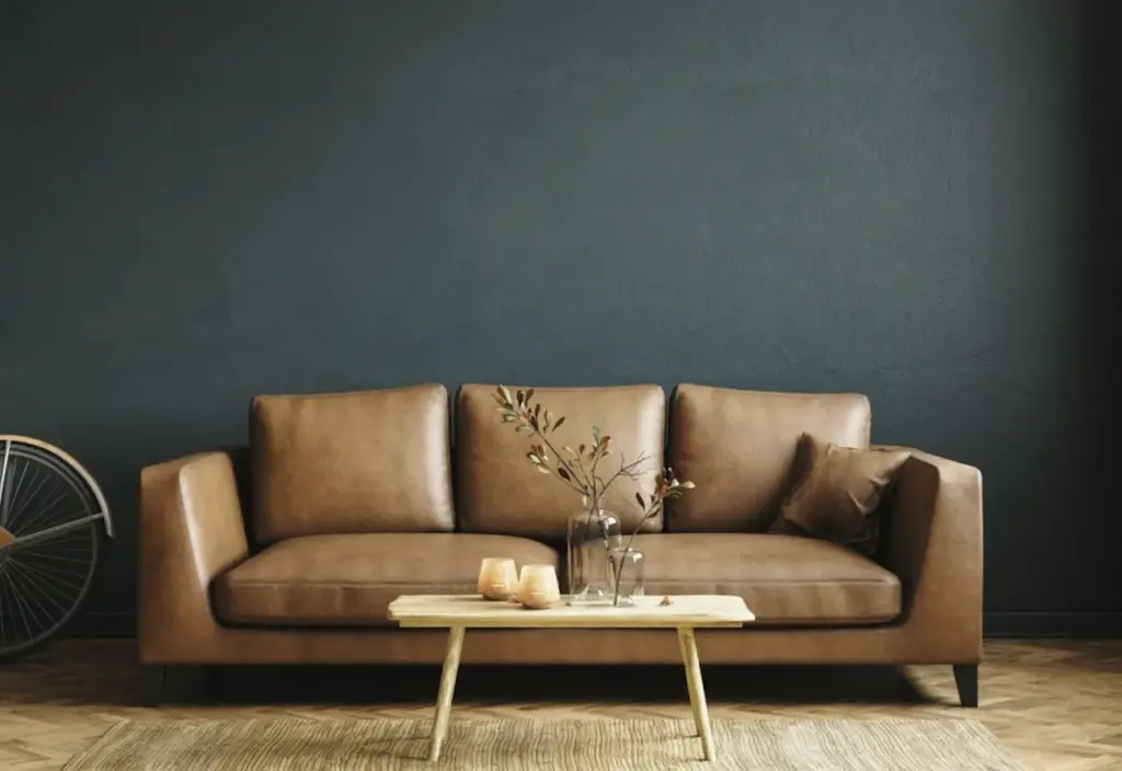 Tan leather sofa with a wooden coffee table against a dark green wall