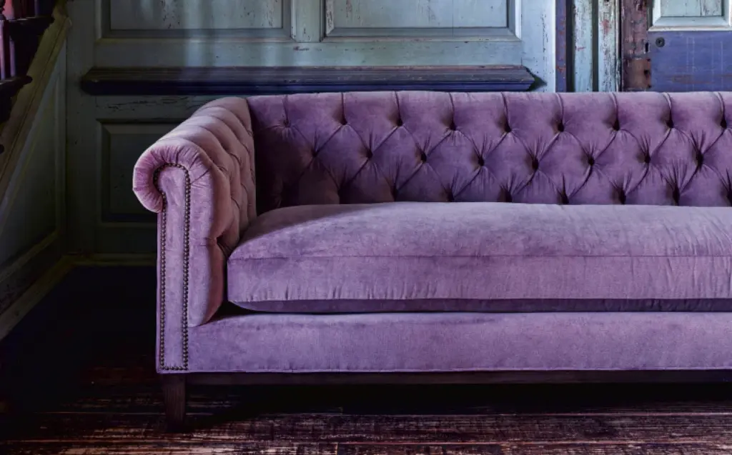Deep button-tufted velvet sofa with rolled arms and piped edges against dark wood paneling