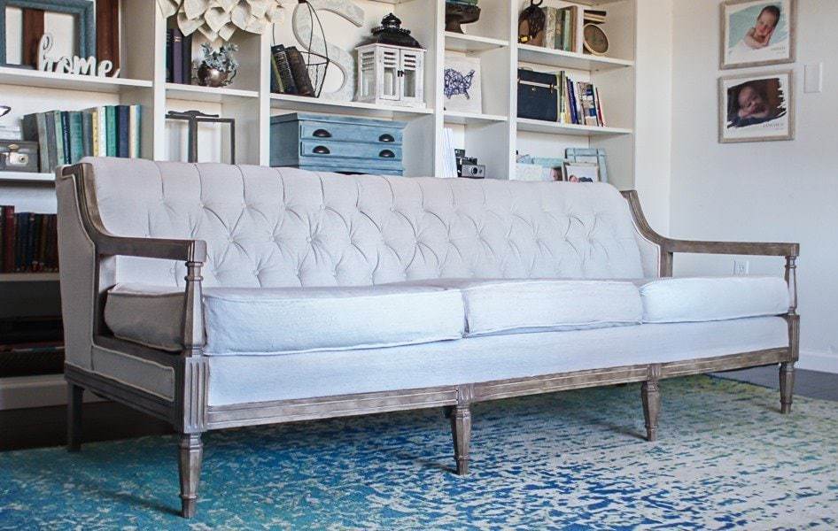 Long sofa with button-tufted back, upholstered arms and exposed wood frame