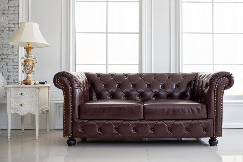 Brown leather Chesterfield sofa with deep button tufting and nailhead trim in a bright room