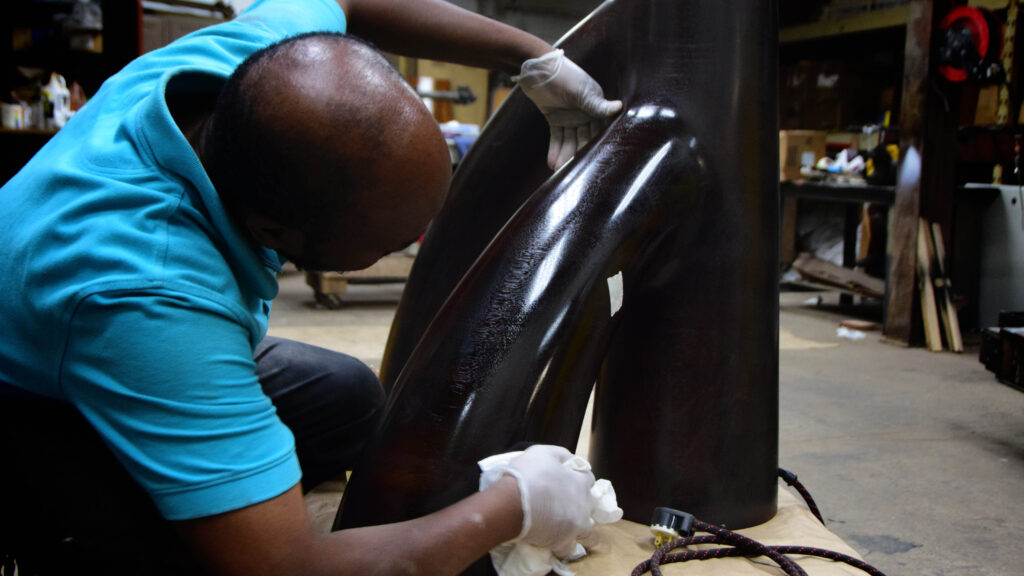 Olek craftsman in gloves hand-finishing a curved dark wood furniture frame in the workshop