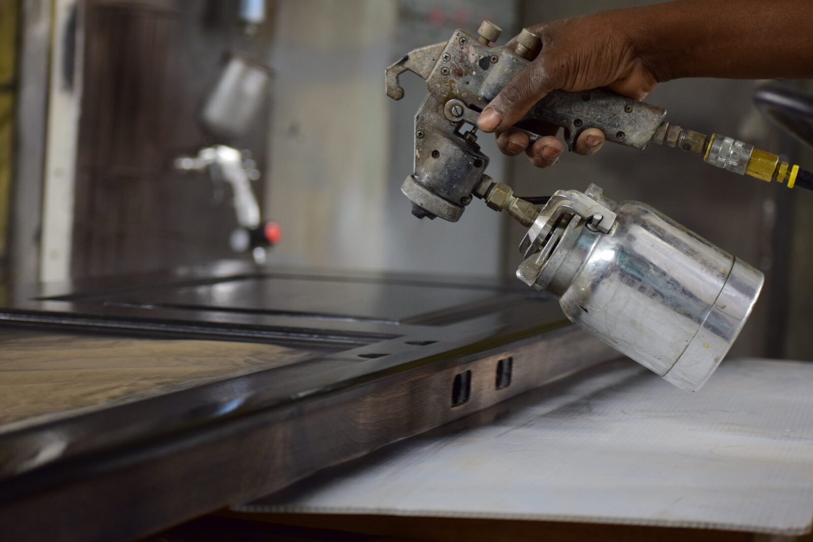 Spray gun applying finish to a dark wood panel in the finishing room